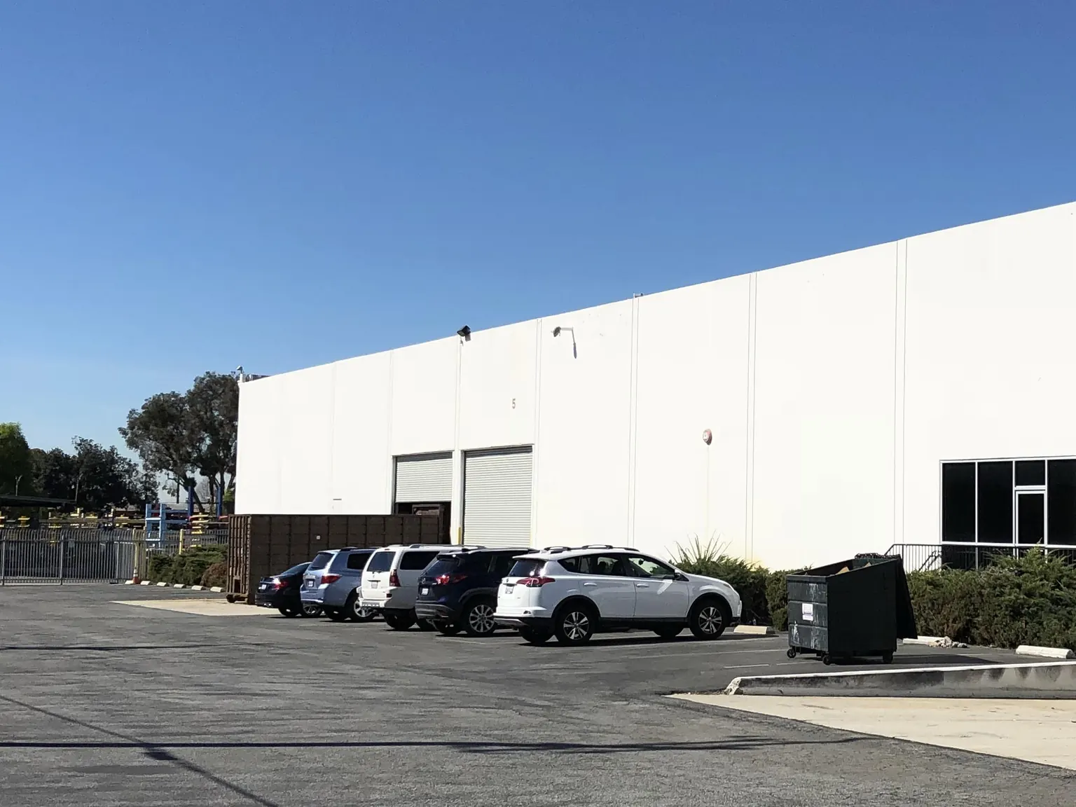 Industrial building at 8616 E Slauson Ave in Pico Rivera with a loading wall, a parking lot, and a dumpster